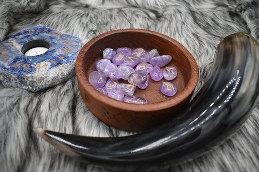 decorative photo of amethyst elder futhark runes in a bowl on an altar with Viking drinking horn and sodalite candle holder