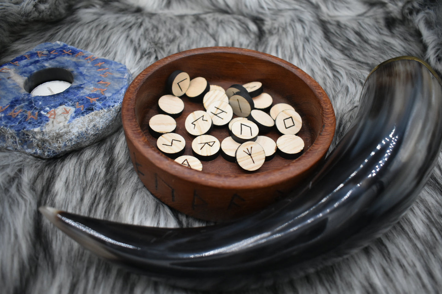 decorative photo of circle laser cut ash runes in a bowl on an altar with Viking drinking horn and sodalite candle holder