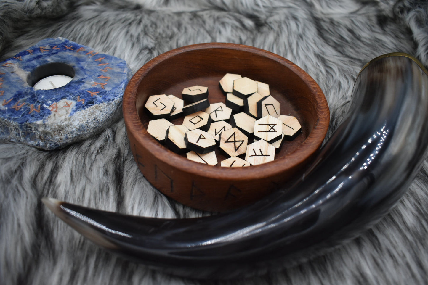 decorative photo of laser cut ash runes in a bowl on an altar with Viking drinking horn and sodalite candle holder