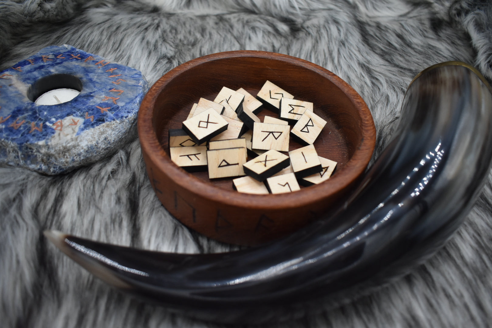 decorative photo of laser cut rectangle ash runes in a bowl on an altar with Viking drinking horn and sodalite candle holder