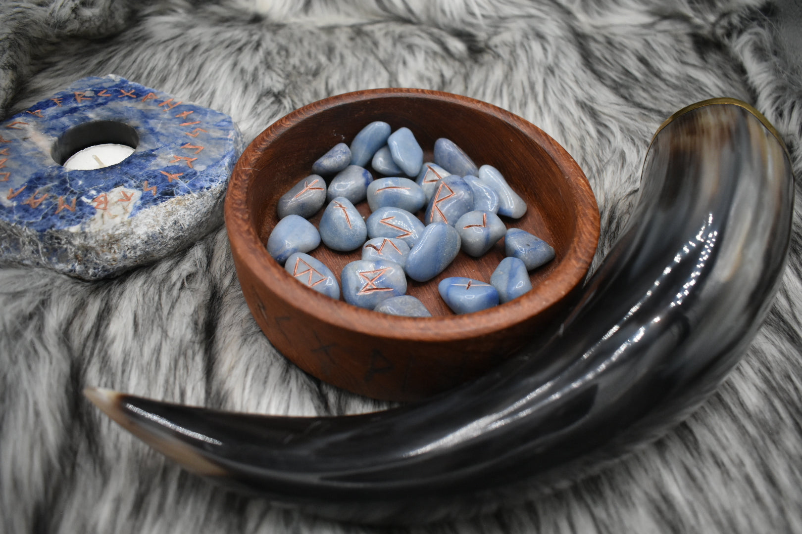 decorative photo of blue aventurine elder futhark runes in a bowl on an altar with Viking drinking horn and sodalite candle holder