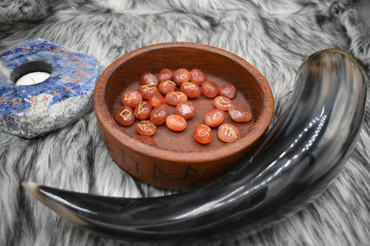 decorative photo of carnelian elder futhark runes in a bowl on an altar with Viking drinking horn and sodalite candle holder