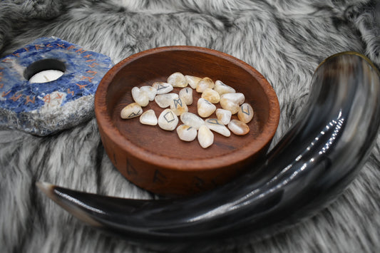 decorative photo of citrine elder futhark runes in a bowl on an altar with Viking drinking horn and sodalite candle holder