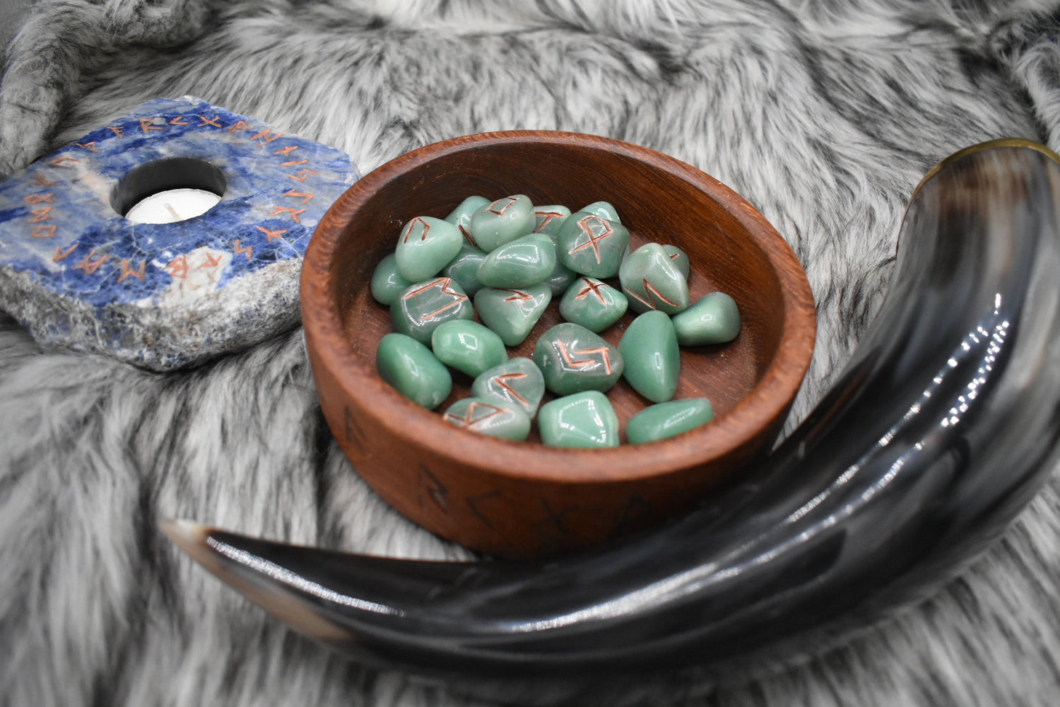 decorative photo of green aventurine elder futhark runes in a bowl on an altar with Viking drinking horn and sodalite candle holder