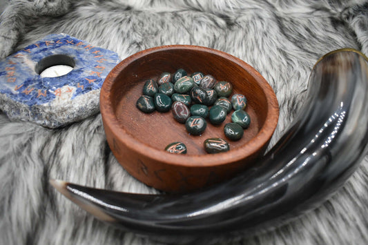 decorative photo of bloodstone elder futhark runes in a bowl on an altar with Viking drinking horn and sodalite candle holder