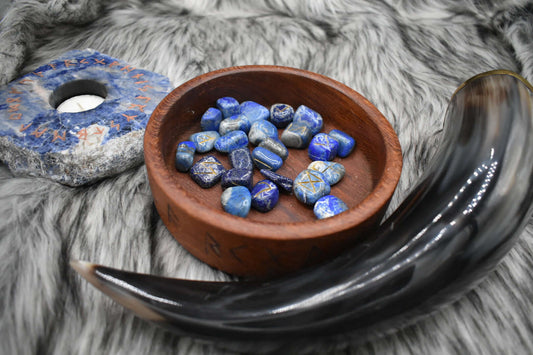 decorative photo of lapis lazuli elder futhark runes in a bowl on an altar with Viking drinking horn and sodalite candle holder