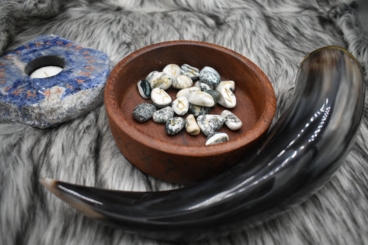 decorative photo of moss agate elder futhark runes in a bowl on an altar with Viking drinking horn and sodalite candle holder