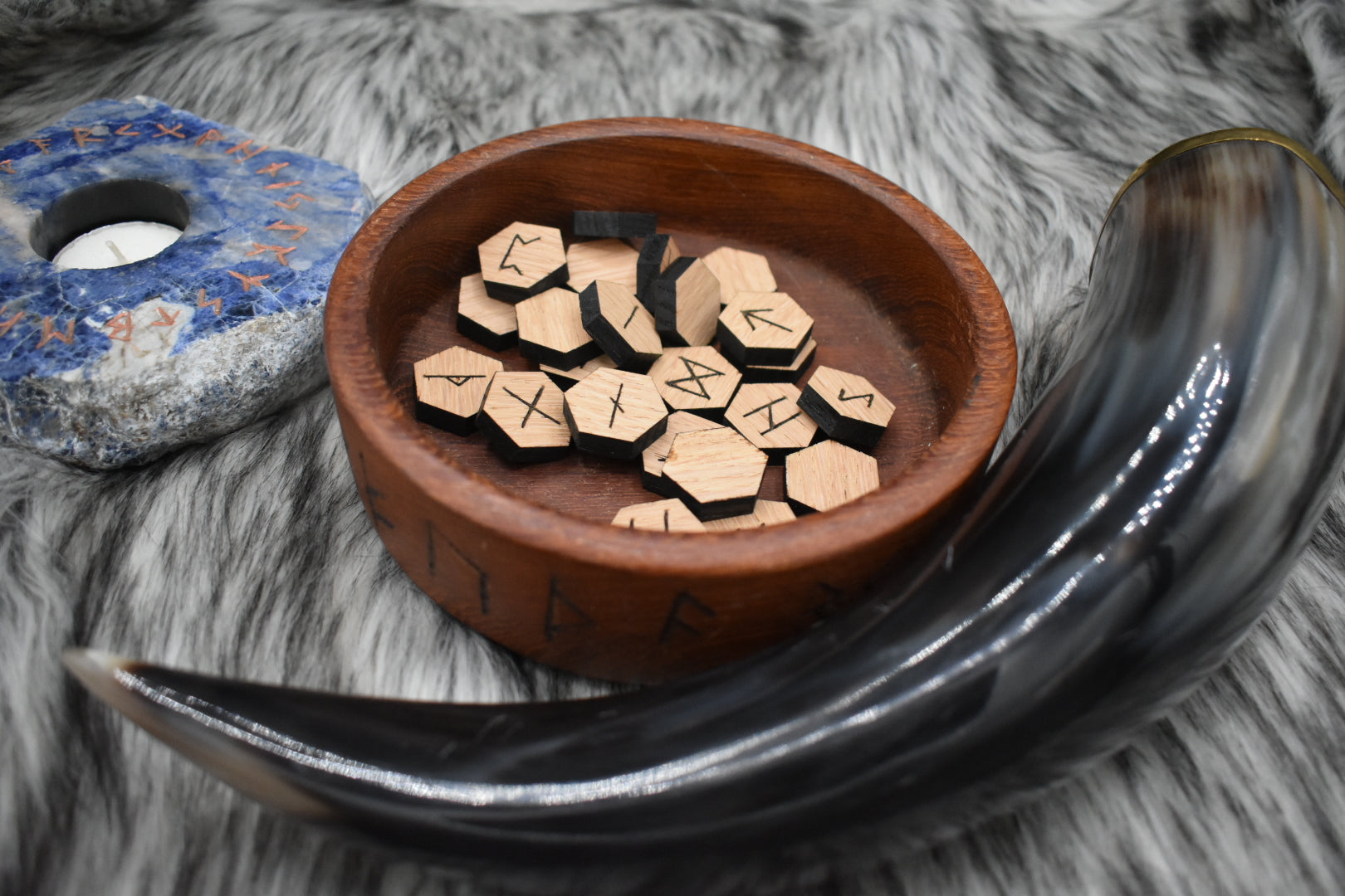 decorative photo of laser cut oak runes in a bowl on an altar with Viking drinking horn and sodalite candle holder