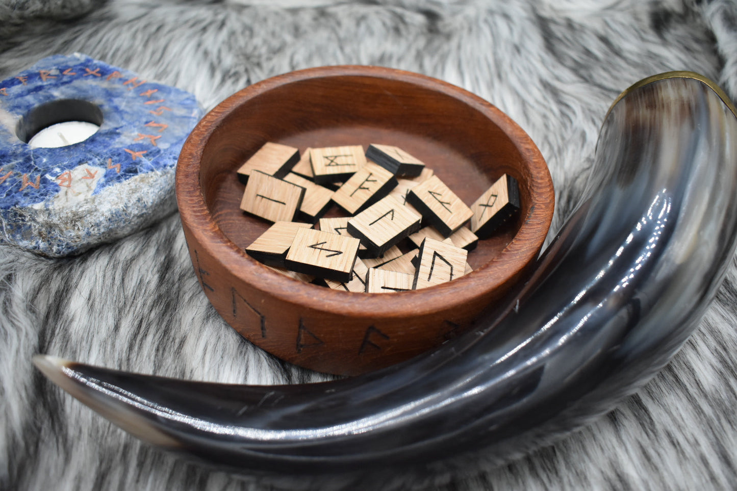 decorative photo of laser cut triangle oak runes in a bowl on an altar with Viking drinking horn and sodalite candle holder