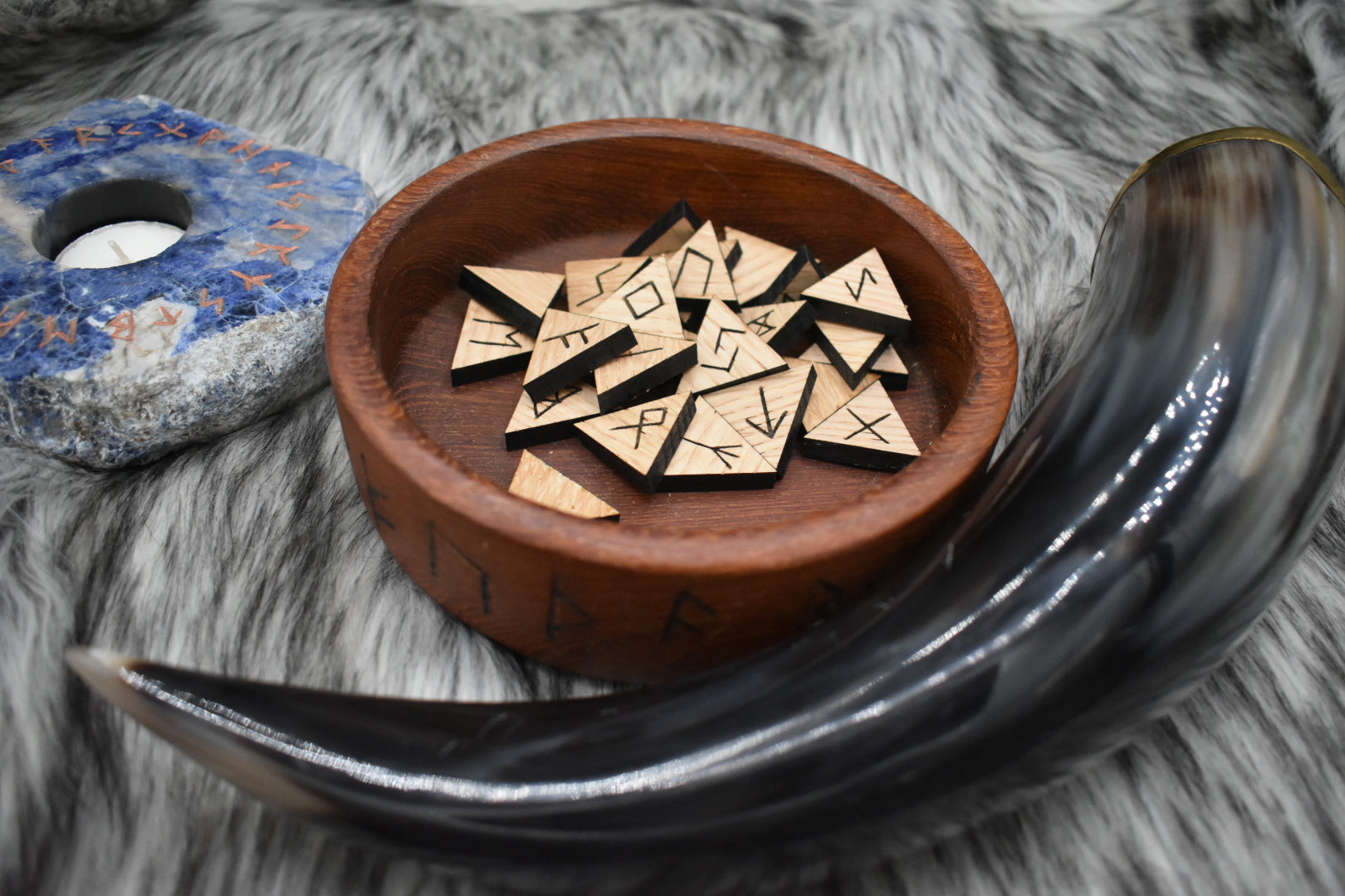 decorative photo of laser cut oak runes in a bowl on an altar with Viking drinking horn and sodalite candle holder