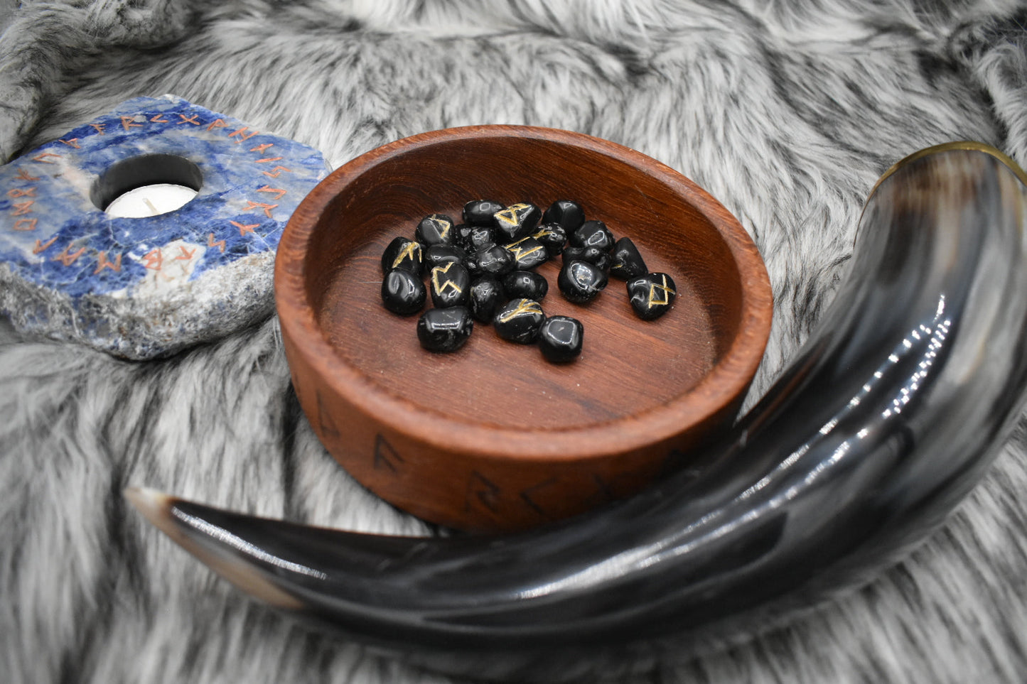 decorative photo of onyx elder futhark runes in a bowl on an altar with Viking drinking horn and sodalite candle holder