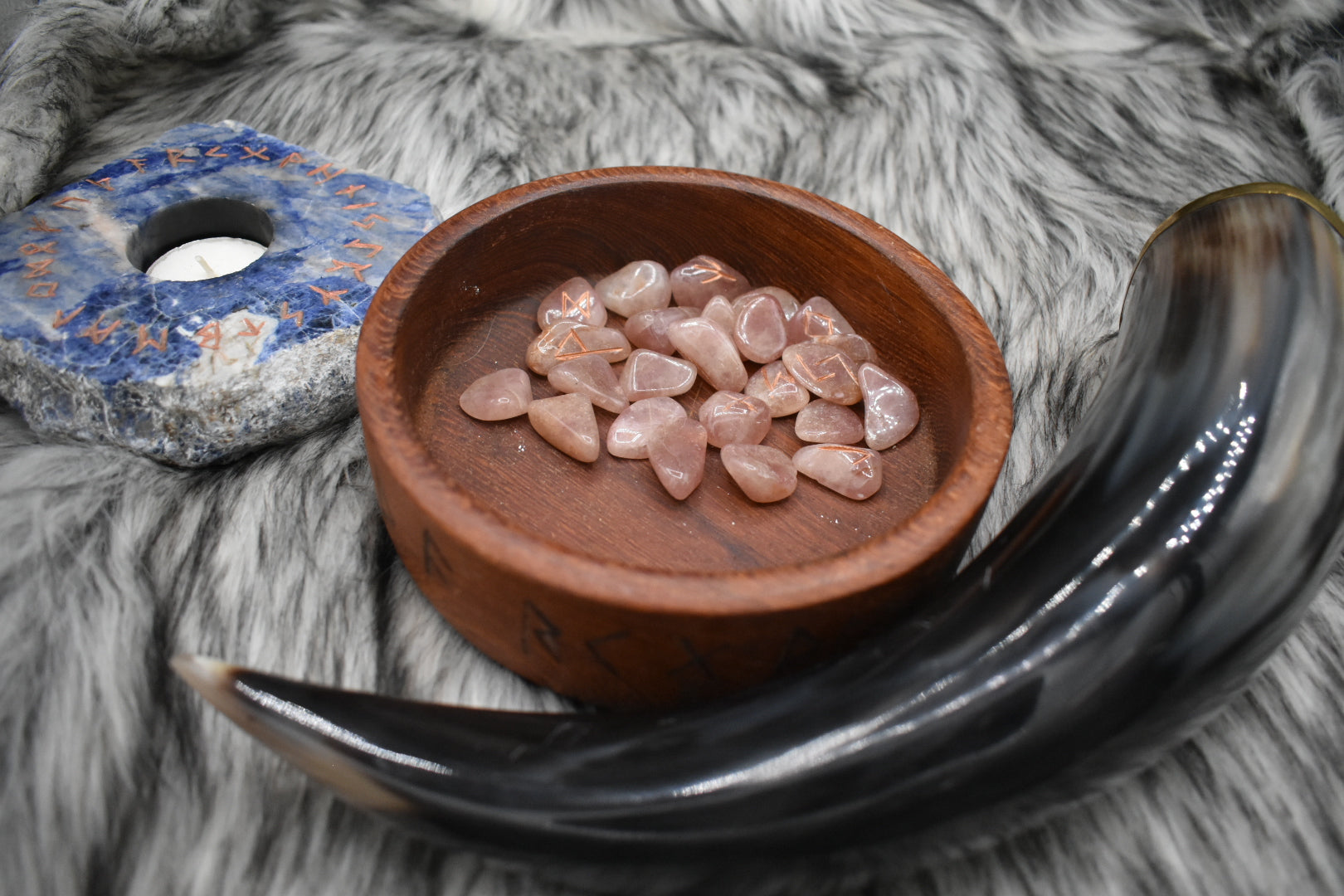 decorative photo of red aventurine elder futhark runes in a bowl on an altar with Viking drinking horn and sodalite candle holder