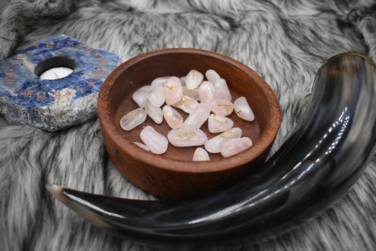 decorative photo of rose quartz elder futhark runes in a bowl on an altar with Viking drinking horn and sodalite candle holder