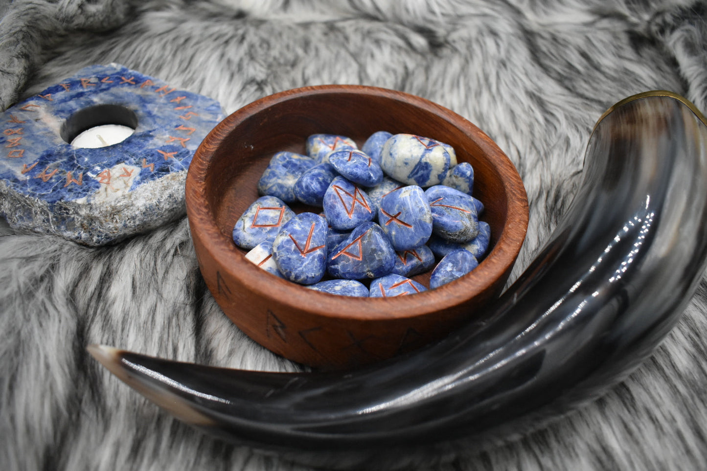 decorative photo of sodalite elder futhark runes in a bowl on an altar with Viking drinking horn and sodalite candle holder