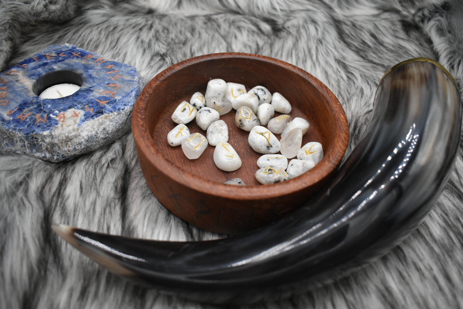 decorative photo of tourmalinated quartz elder futhark runes in a bowl on an altar with Viking drinking horn and sodalite candle holder