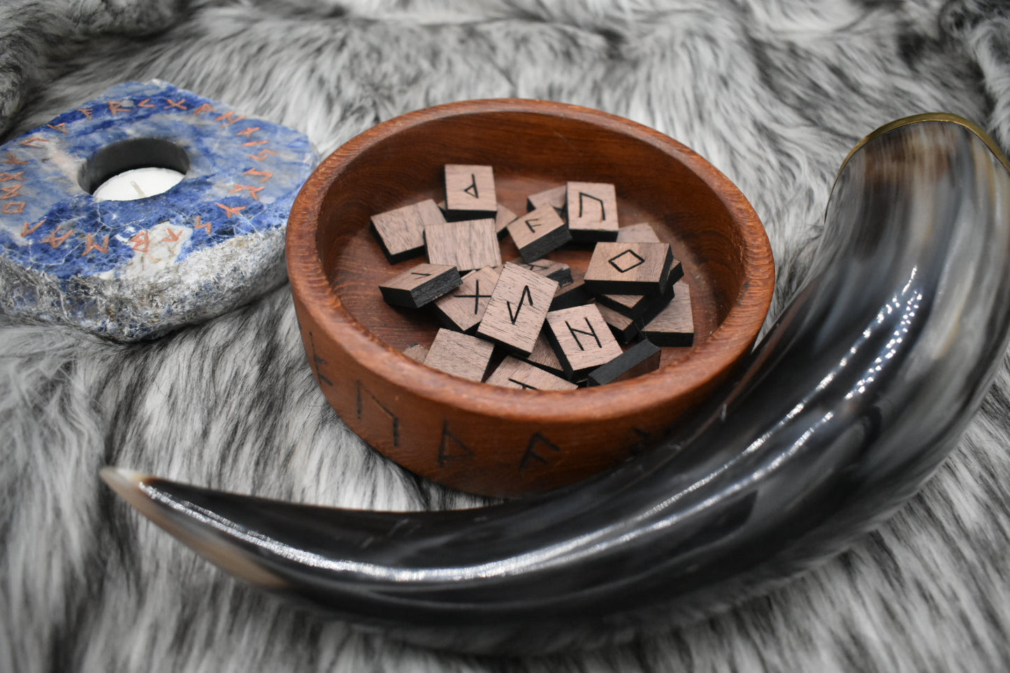 decorative photo of laser cut rectangle walnut runes in a bowl on an altar with Viking drinking horn and sodalite candle holder